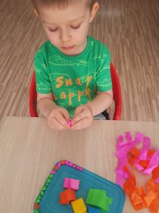 Kilkuletni chłopiec w zielonej koszulce siedzi przy stole, wykonuje kolorowe kulki z bibuły.